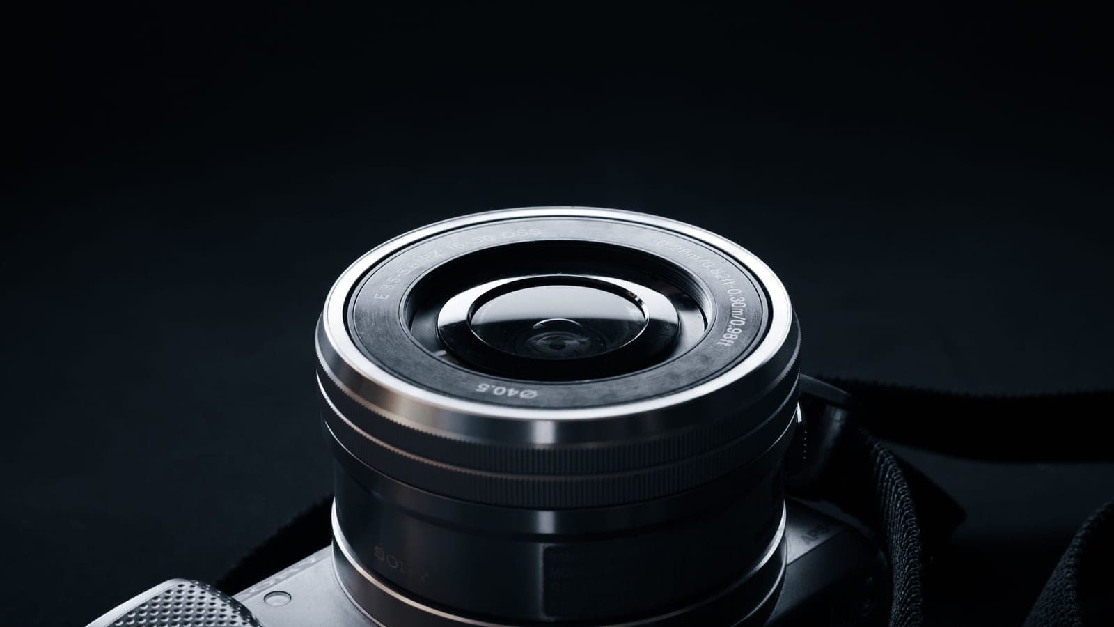 A camera lens rises from a camera body against a dark background.