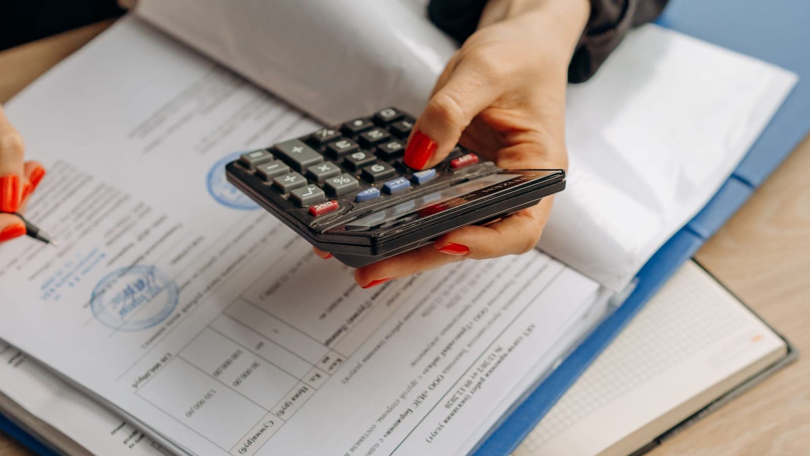 A person holds a calculator above financial documents on a desk.