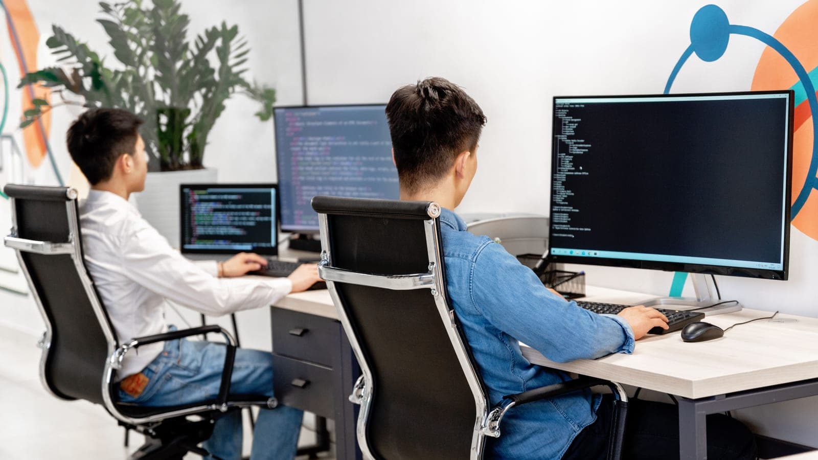 Two developers seated at desks facing monitors displaying code.